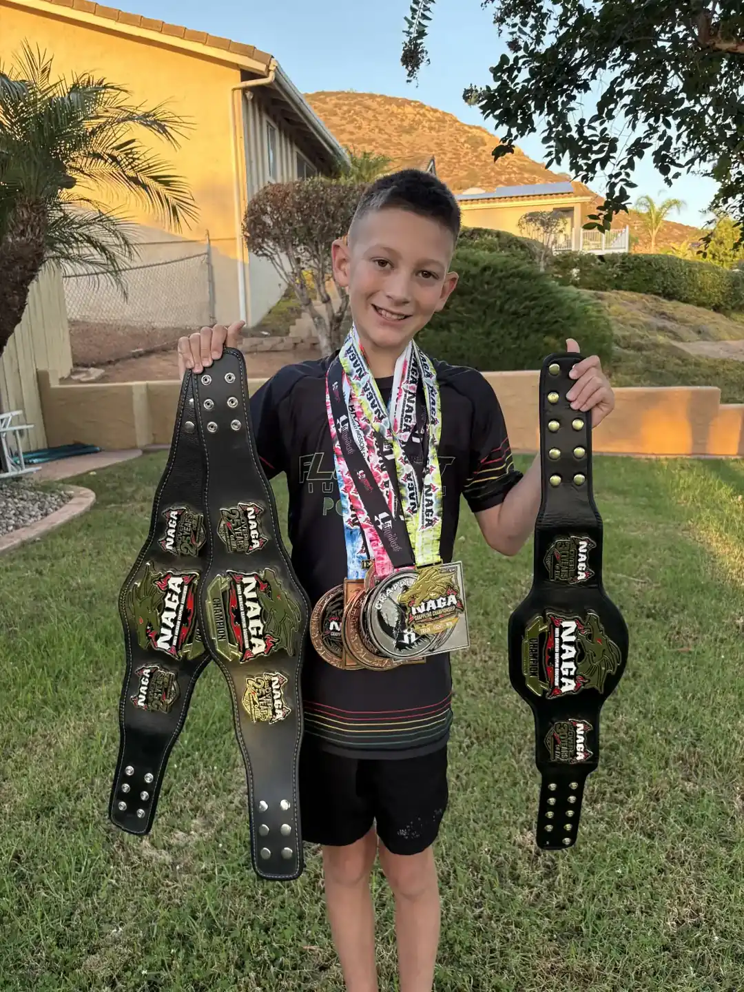 Roman Chagala Jiu Jitsu competitor displaying his NAGA championship belts and medals outdoors